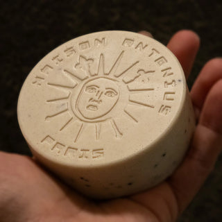 Oatmeal soap with honey and orange essential oils with sun design and engraved text held in a hand against a dark background